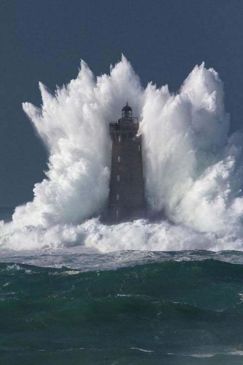Fotografía de una ola chocando con una torre en el mar 