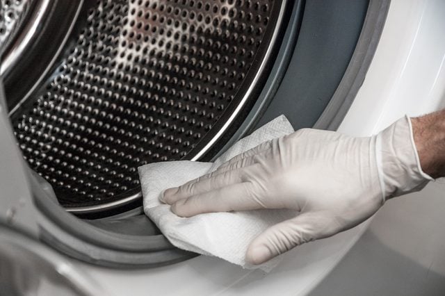 mano con un guante blanco limpiando las gomas de la carga de una lavadora 