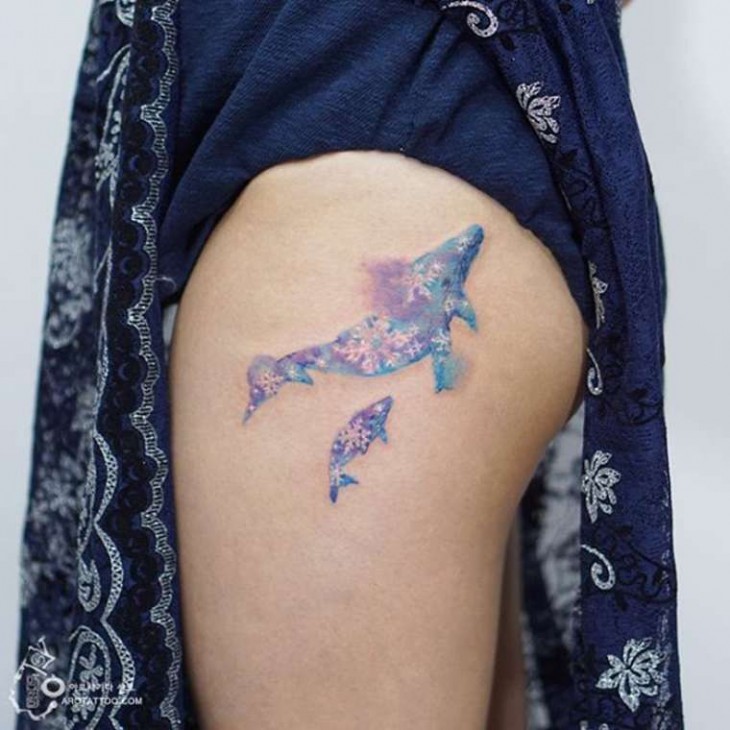 Tatuaje acuera con el diseño de unos delfines sobre el muslo de una mujer 