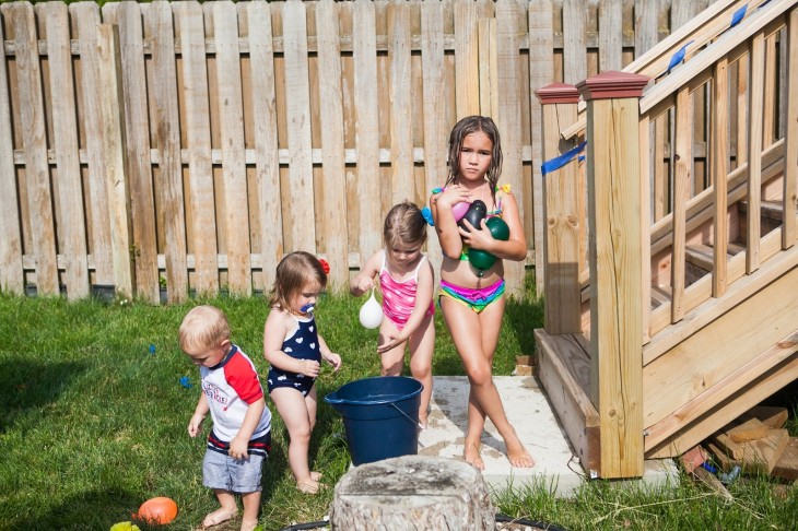 fotografía de cuatro niños en traje de baño con globos llenos de agua 