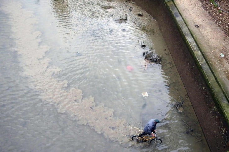 hombre sacando una bicicleta de un canal contaminado en parís 