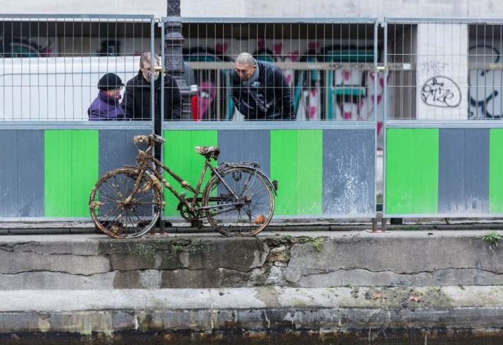personas a la orilla del canal Saint-Martin en París viendo una bicicleta abandonada 
