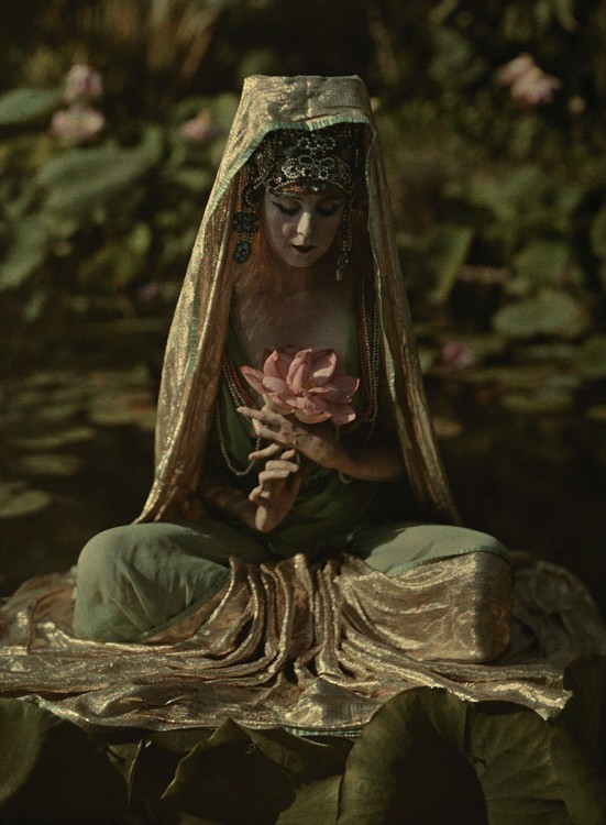 Woman adorned like a Chinese goddess poses in a garden in California, 1915.