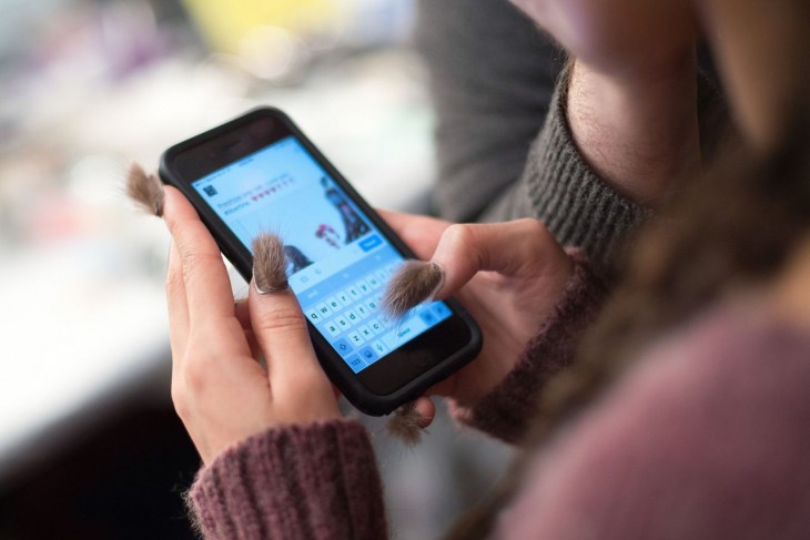 manos de una chica con un celular usando uñas peludas 