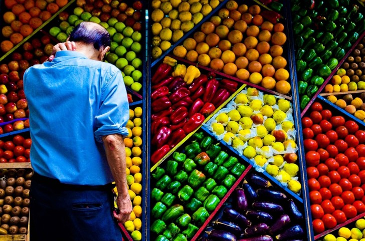 hombre viendo hacia un estante lleno de frutas y verduras perfectamente ordenadas 