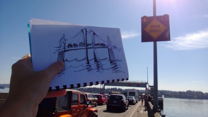 fotografía de una persona mostrando el dibujo de un puente mientras está en un embotellamiento 