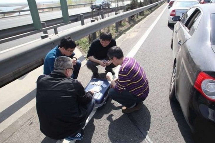 Chicos jugando cartas sobre una maleta en medio de un embotellamiento 