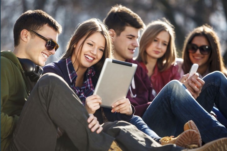 Grupo de 5 chicos con tablets y celulares en sus manos 