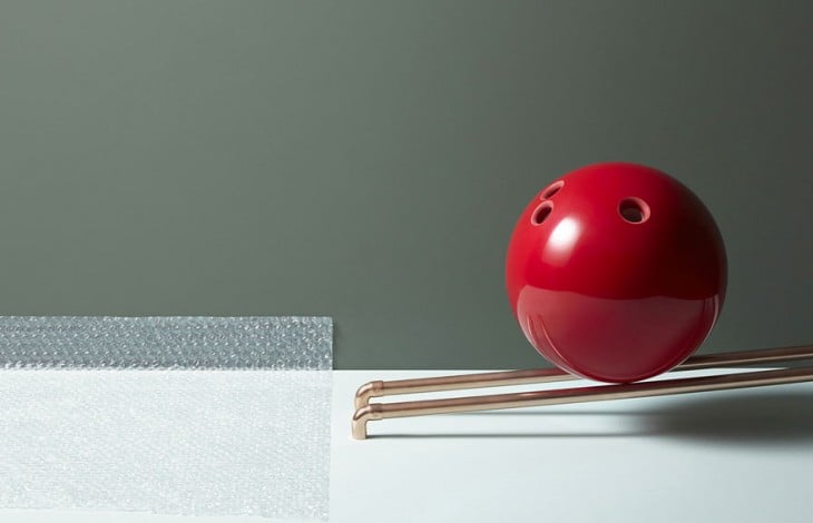 Fotografía de una bola de boliche roja sobre dos tubos a punto de caer 