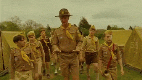 Gif de niños vestidos de boy scout caminando en medio de un campamento 