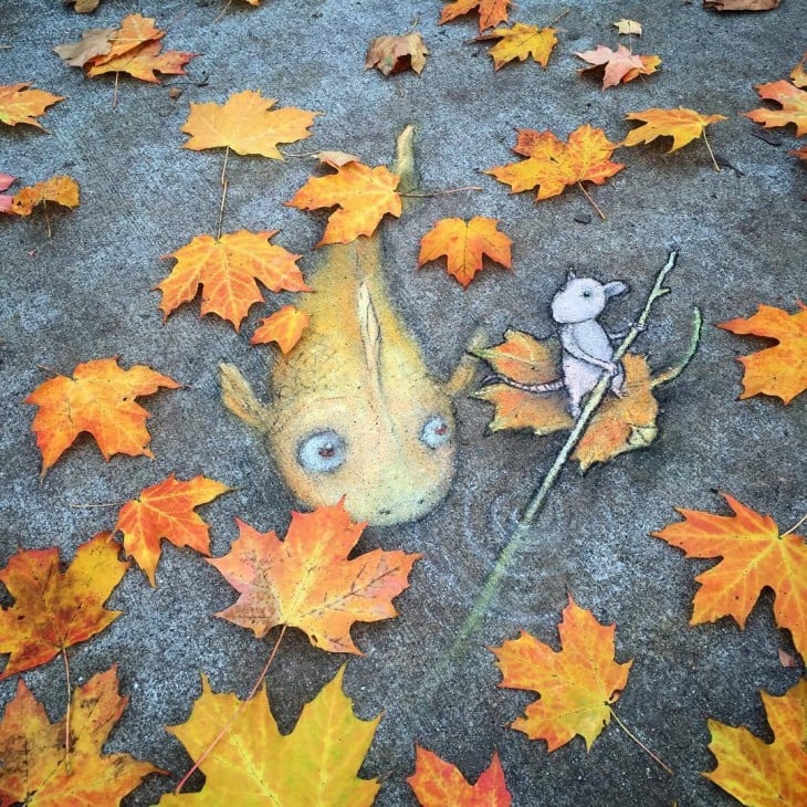 David Zinn creo una obra de arte en el suelo de un pez con un ratón interactuando con hojas secas en el suelo 