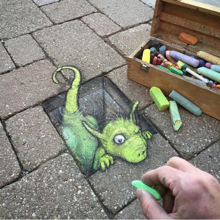 David Zinn dibujo con tiza en una calle un dibujo de un dragón saliendo de una banqueta 