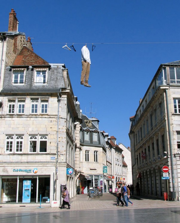 escultura en forma de un cuerpo real colgado entre dos edificios 