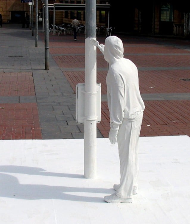 Impresionantes escultura callejera de una persona pintando un poste de color blanco 