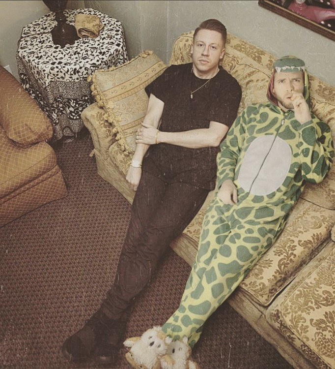 chico vestido de dinosaurio sentado en un sillón a lado de Macklemore 