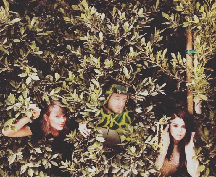 phtoshop de un chico vestido de dinosaurio escondido entre unos arbustos con Taylor Swift y Selena Gomez