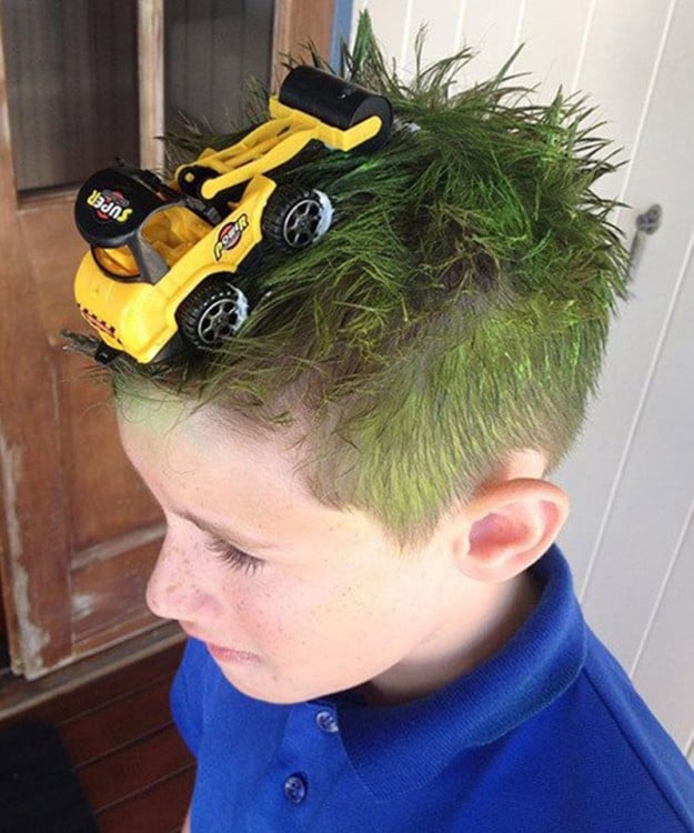 niño con el cabello verde y un tractor de juguete encima de él 