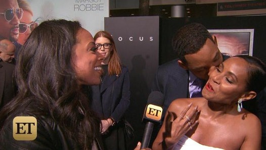 Will Smith abrazando y dando un beso a su esposa Jada Korent Pinkett enfrente de una entrevistadora 