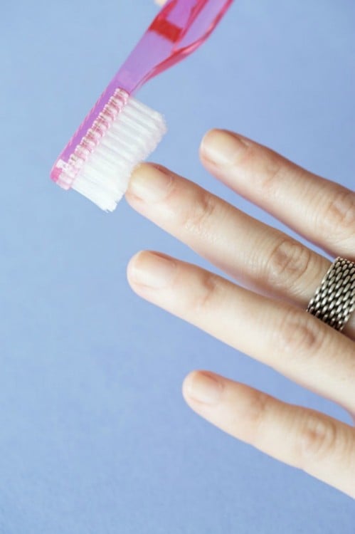 mujer limpiando sus uñas con un cepillo de dientes 