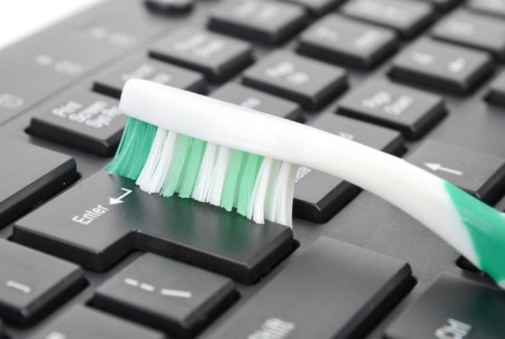cepillo de dientes limpiando entre las teclas de una computadora 