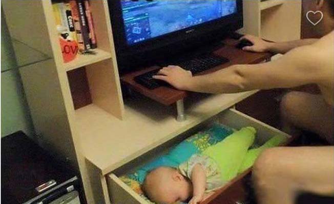 bebé dormido en un cajón mientras su papá juega en la computadora