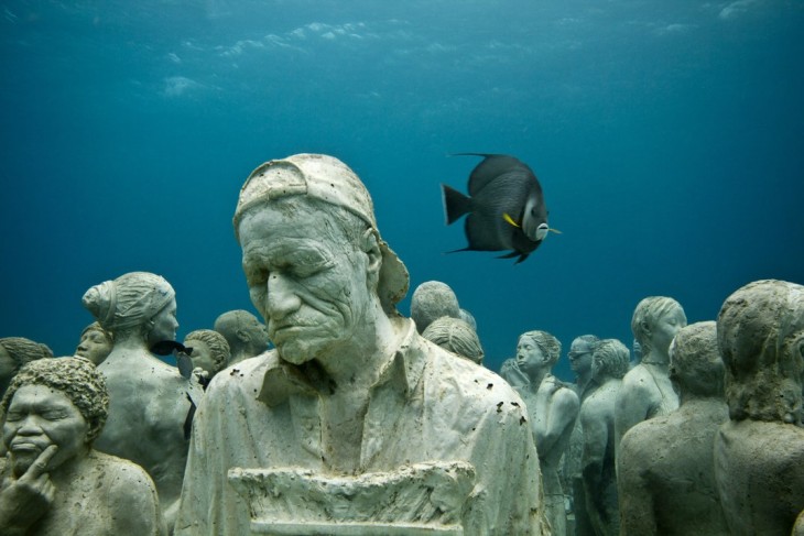 ESCULTURA DE UN HOMBRE MAYO CANSADO BAJO EL AGUA DE LOS ARRECIFES DE CANCÚN