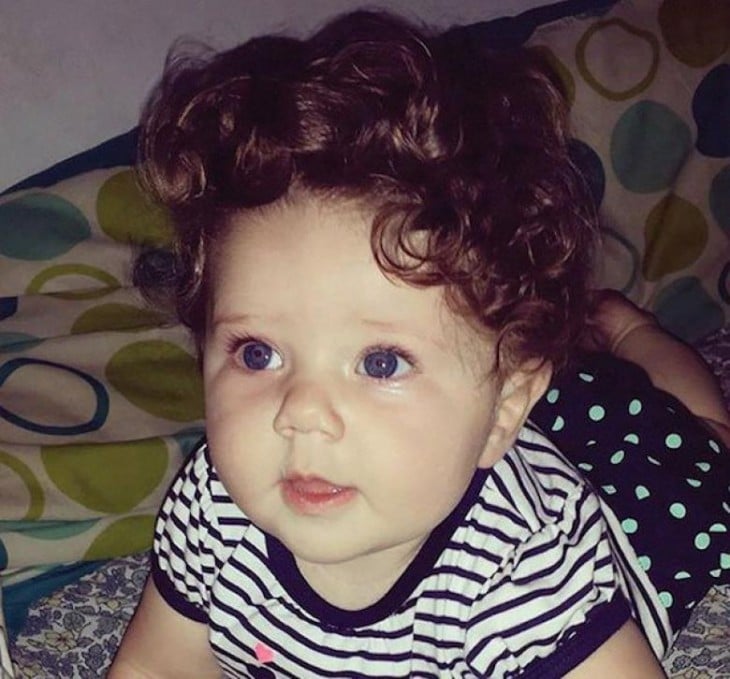 fotografía de una bebe con mucho cabello chino acostada sobre una cama 