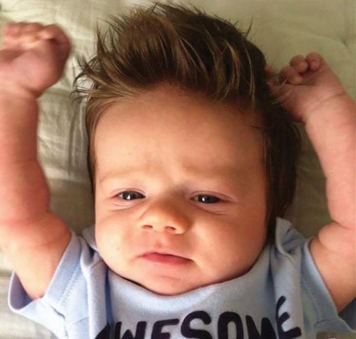 foto de un bebé con mucho cabello acostado con las manos hacia arriba 