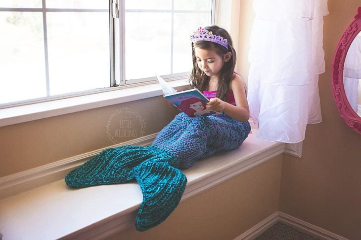 Cola de sirena con una niña leyendo en la ventana