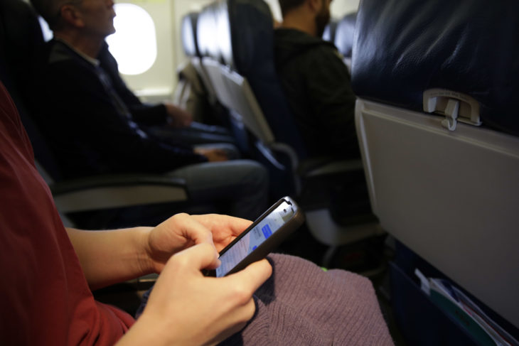 mujer sentada en un avión mensajeando con un celular 