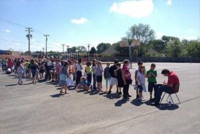 niños hacen fila para que el conserje de su escuela les firme su anuario