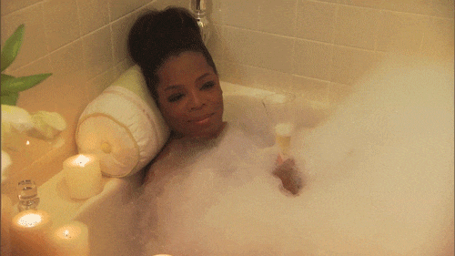 oprah relajada en una tina con burbujas y velas y una copa de champagne