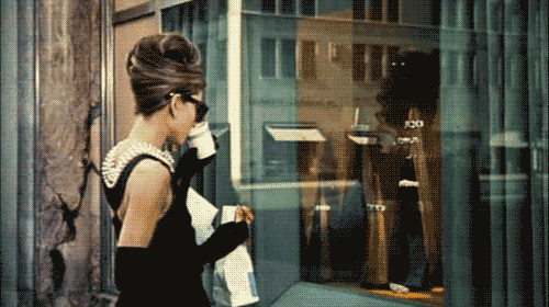 Gif de una escena de una chica tomando café mientras ve detrás de un aparador 