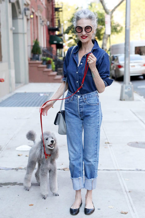 Mujer de +60 años vestida muy trendy con ropa de mezclilla mientras pasea a su perro Poodle