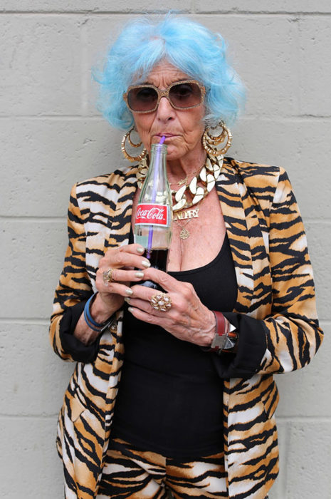 Mujer de +60 años tomando una coca con el cabello azul vestida a la moda