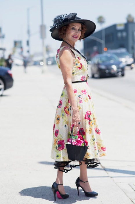 Mujer de +60 años muy guapa con un vestido floreado, sombrero negro, zapatos negros altos