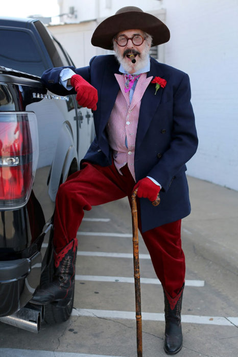 Hombre de +60 años con sombrero, puro, guantes rojos, pantalón rojos, botas, saco azul y camisa rosada