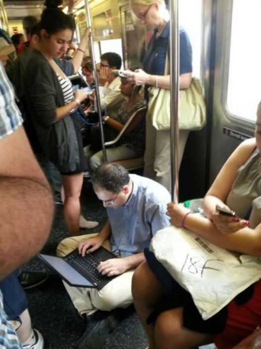 Hombre sentado en el piso del metro con su computadora