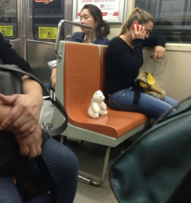 Mujer en el metro hablando por teléfono, el asiento del lado va ocupado por su oso de peluche