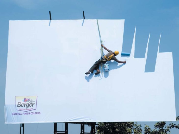 Hombre pintando un espectacular pero da la impresión que está pintando el cielo