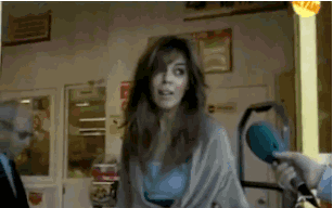 GIF de mujer dando una entrevista en el portal de una puerta eléctrica, pero ésta se cierra mientras habla y la golpea