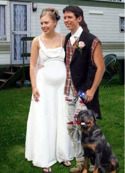 Foto de novios. La novia está embarazada, con sandalias y un cigarro, el novio con pantalones rotos, chimuelo y una cerveza. Atrás se ve una casa remolque y en la foto aparece un perro