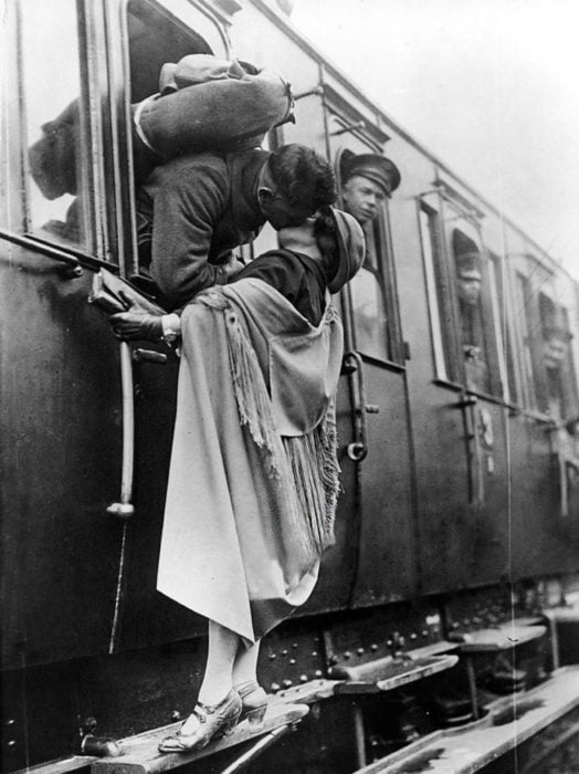 Amor en tiempos de guerra. soldado sale de la ventanilla del tren para besaar a una mujer que está en el escalón de la parte de afuera del tren