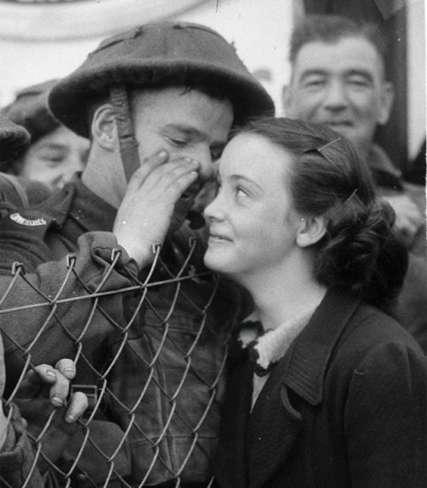 Amor en tiempos de guerra. un soldado le susurra algo a una mujer mientras ésta sonríe