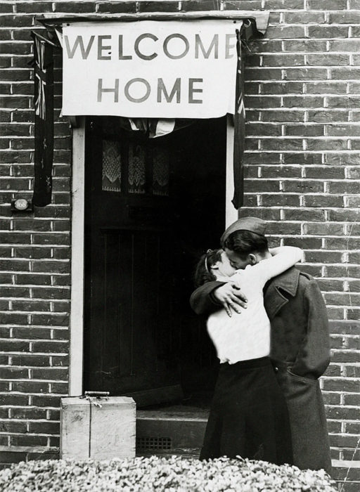 Amor en tiempos de guerra. soldado y mujer se besan en la puerta de una casa que tiene un letrero de welcome home