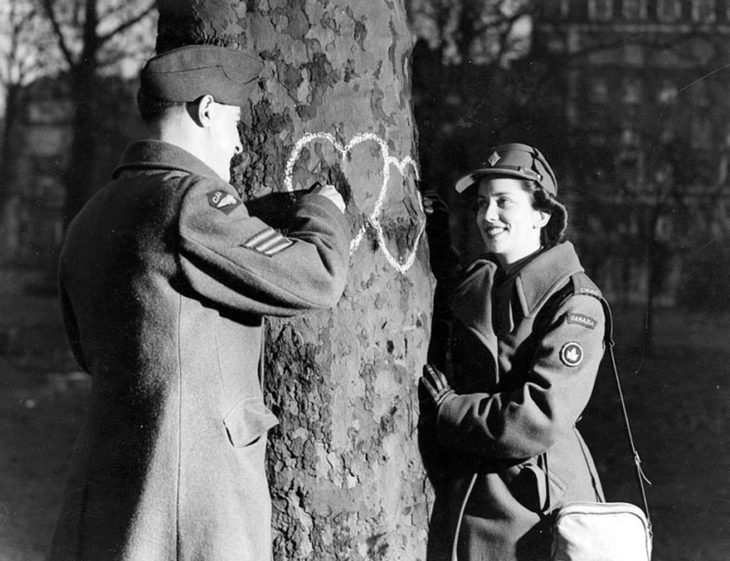 Amor en tiempos de guerra. soldado y mujer marcan dos corazones en un arbol