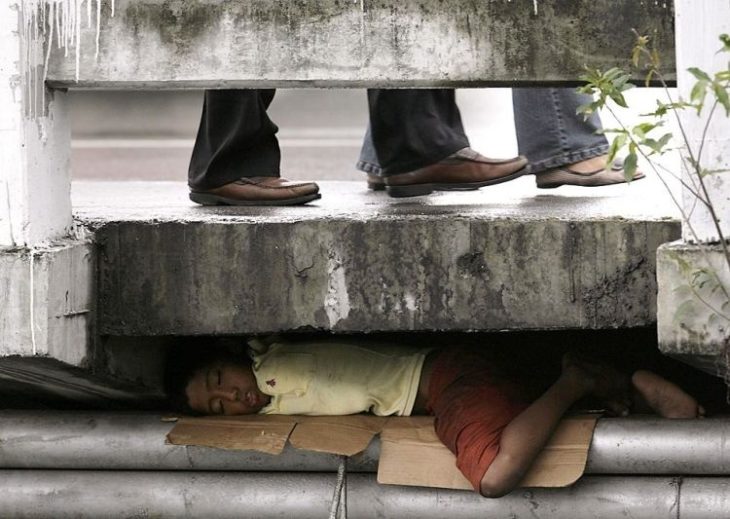 niño bajo la banqueta tratando dormir y pasando frio