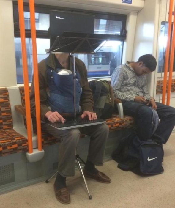 hombre con su computadora y un tripode en medio del metro con su bebpe en el cangurero que trae cargado