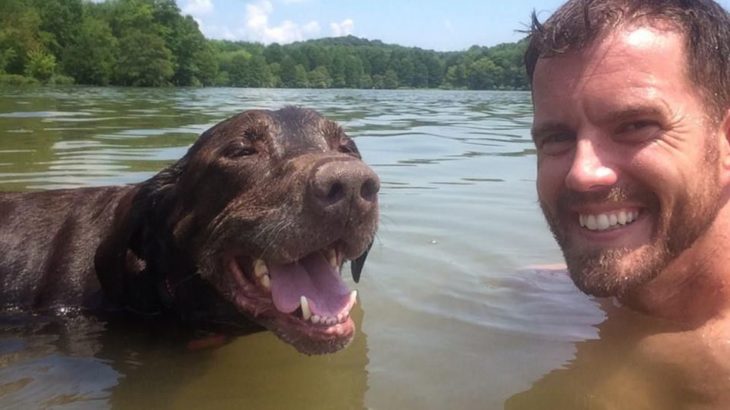 Perra labrador y hombre sonriendo a la cámara mientras nadan juntos