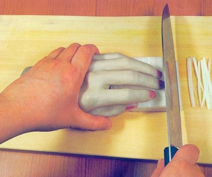 Persona sosteniendo una mano de plastico que a la vez sostiene una barra de algo que se està cortando con un cuchillo